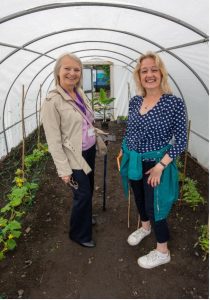 Two people standing in a polytunnel leaning on spades.